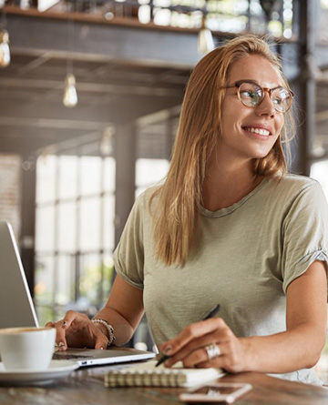 happy female copywriter writes ideas in notepad and searches information on laptop computer spends