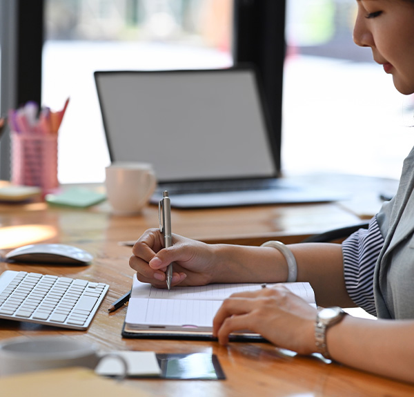 Businesswoman sitting at her office desk and making notes on notebook.